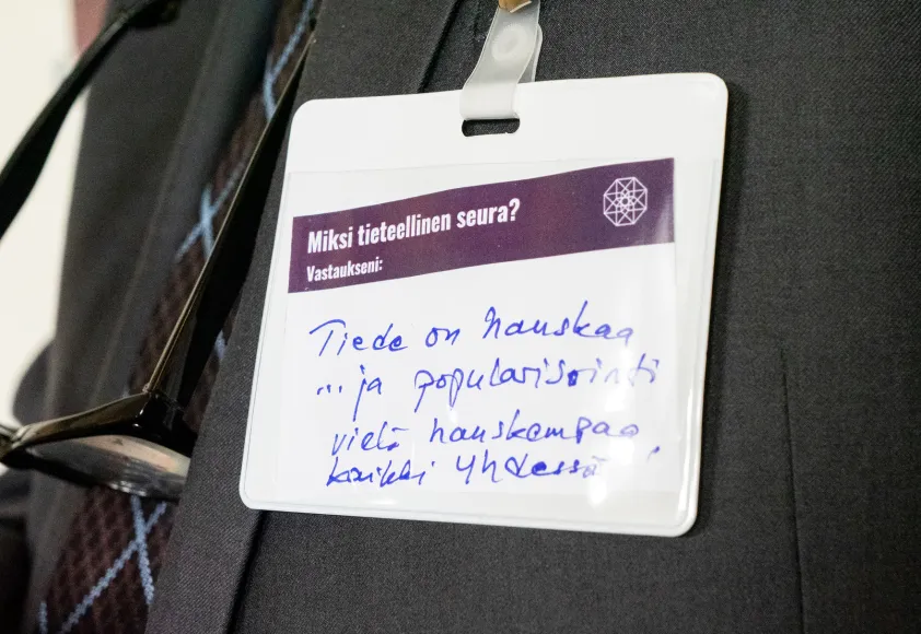 Puvun rintapielessä on pienessä muovitaskussa lappu, jossa on käsin kirjoitettua tekstiä.