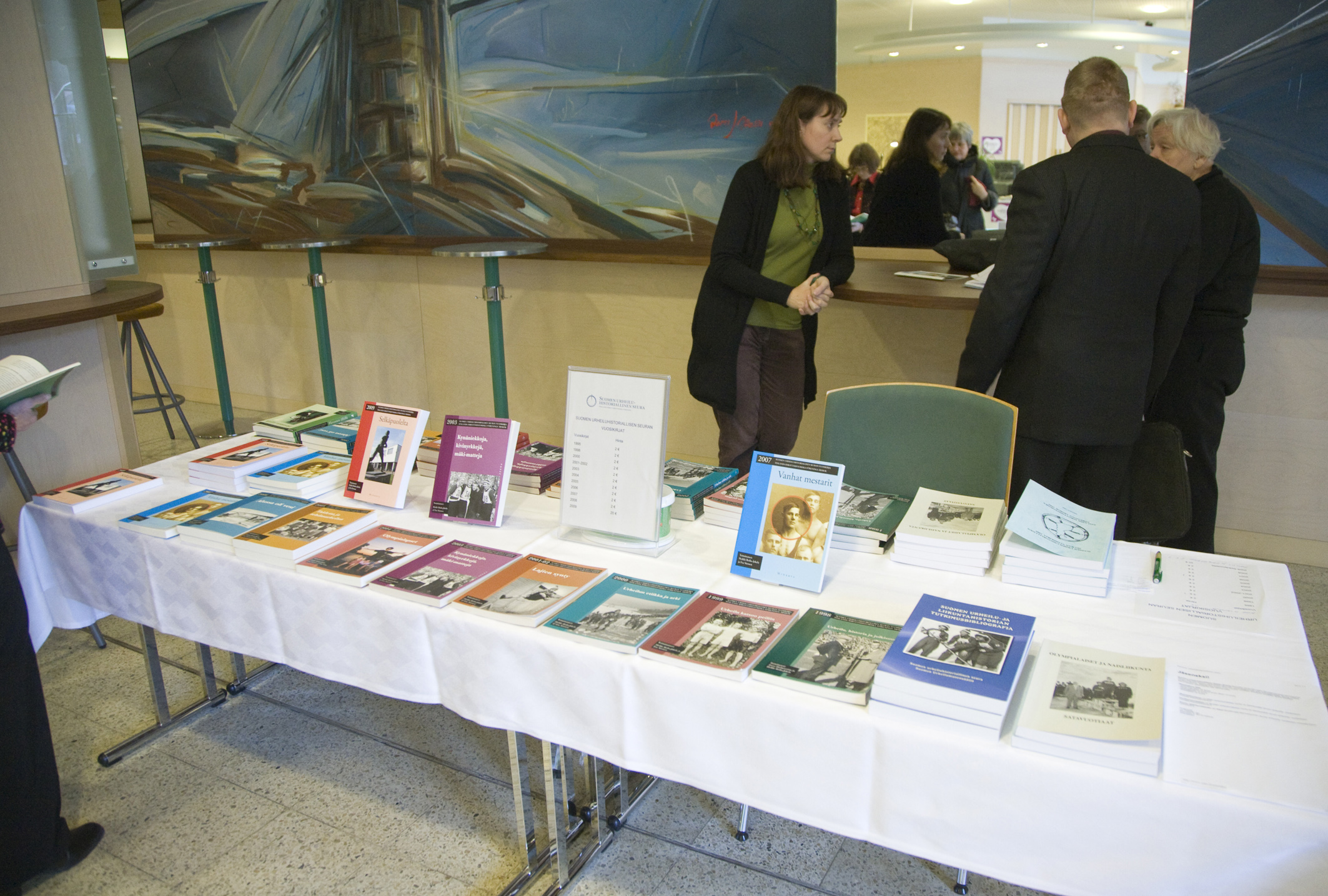 Tre personer står och diskuterar sinsemellan bakom ett bord på vilket publikationer är utställda.