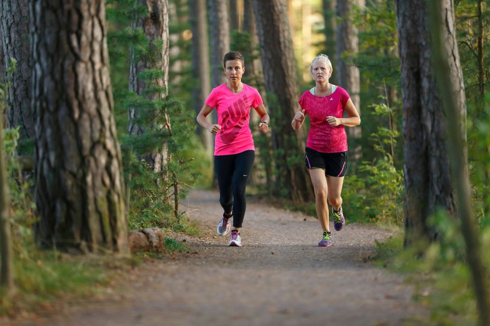 Kaksi henkilöä lenkkeilee metsäpolulla.