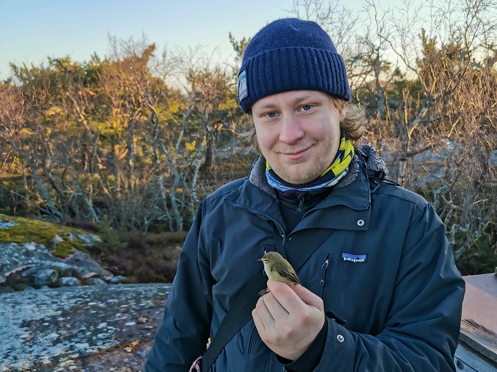 Henkilö ulkoilmassa, kädellään pieni lintu.