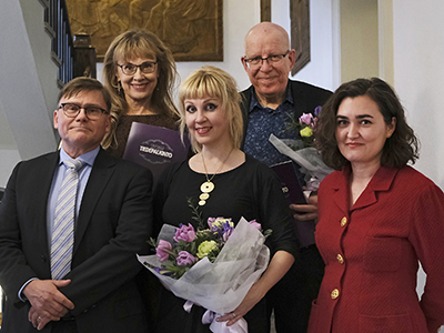 Viisi hymyilevää henkilöä, kolme naisoletettua ja kaksi miesoletettua.