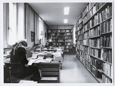 Arkistohuoneen pöydän ääressä istuu henkilö, joka on syventynyt tutkimustyöhön.