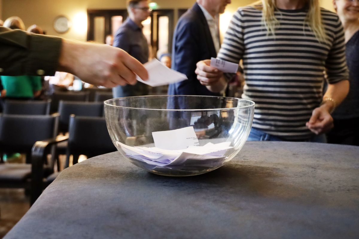 Folk sätter röstsedlar i en genomskinlig skål.