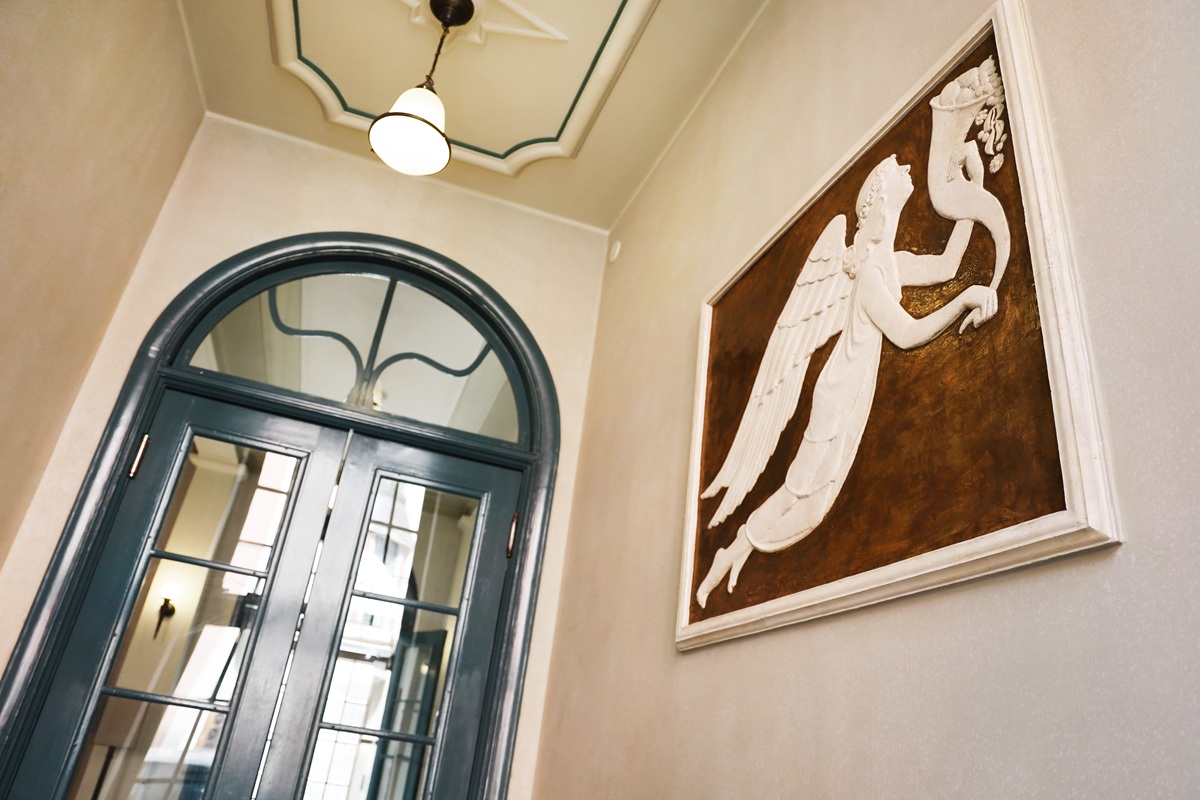 Suuret ovet sekä seinällä suuri taulu, jossa on valkoinen torvea soittava enkeli.