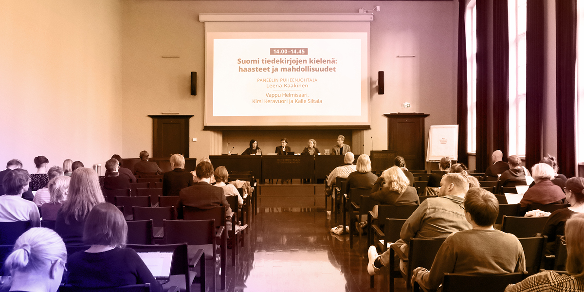 Ihmisiä suuressa salissa kuuntelemassa neljää puhujaa.